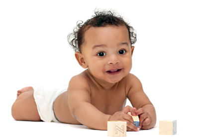 Imagem: Fotografia. Uma bebê morena, deitada de barriga para baixo, sem roupa, com fralda branca no corpo, cabelos pretos, e perto dela, peças de brinquedos. Fim da imagem.
