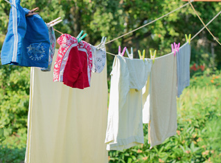 Imagem: Fotografia. À frente, dois varais com roupas coloridas : um short pequeno azul, outro em vermelho, outras duas pessoas em bege e blusa pequena de cor azul-claro e no outro varal, toalha bege. Mais ao fundo, vegetação em verde.  Fim da imagem.
