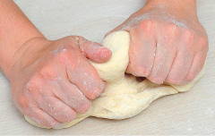 Imagem: Fotografia. Passo 4. Mãos de uma pessoa amassando massa de cor bege-claro. Fim da imagem.