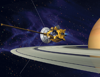 Imagem: Ilustração. Vista parcial de saturno, planeta redondo de cor bege-claro, com anéis ao redor de cor cinza. Sobre os anéis, à esquerda, uma sonda, objeto de cor amarela, pequeno, com parte redondo ao fundo em cinza-claro e uma haste fina na horizontal e linhas finas em branco. Mais ao fundo, céu em azul-escuro com centenas esferas em amarelo.  Fim da imagem.