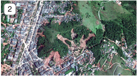 Imagem: Fotografia 2. Vista do mesmo local descrito anteriormente, com cidade à esquerda com casas e prédios e à direita, a parte com vegetação e árvores menores, com mais partes em solo em marrom-claro à direita. Fim da imagem.