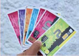 Imagem: Fotografia. Uma pessoa de pele morena, segurando notas de papel colorido em rosa, roxo, laranja, azul-claro e verde-claro com número 2. À esquerda, logotipo escrito: União Sampaio.  Fim da imagem.