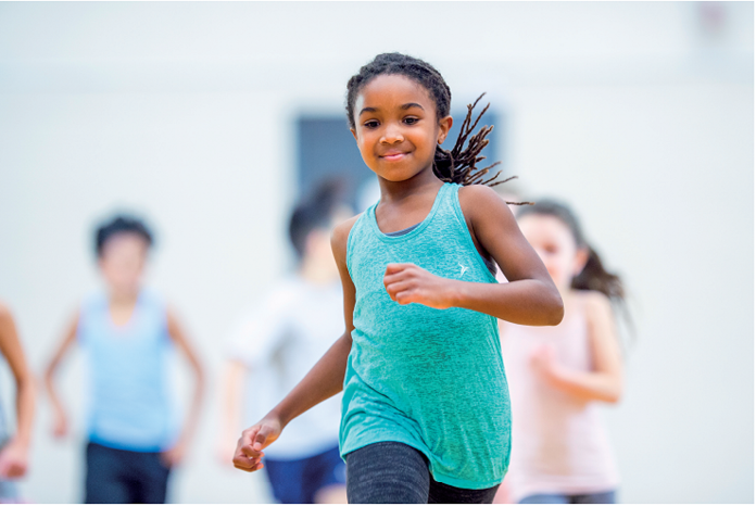 Imagem: Fotografia. Uma criança com cabelos crespos, usando uma blusa regata. Ela está correndo. Atrás, desfocadas, outras crianças correndo. Fim da imagem.