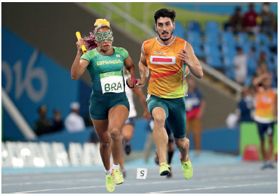 Imagem: Fotografia. Uma mulher uniformizada, com uma venda nos olhos segurando um bastão. Ao lado, um homem uniformizado correndo ao lado dela. Fim da imagem.