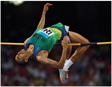 Imagem: Fotografia em preto e branco. Um homem uniformizado saltando de costas sobre uma vara.  Fim da imagem.