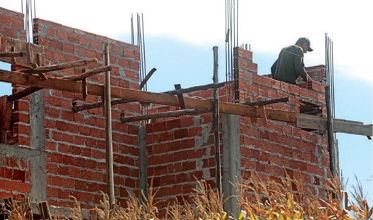 Imagem: Fotografia. Uma pessoa está em pé em uma construção. Em volta dela há paredes de tijolos e cimento. Fim da imagem.