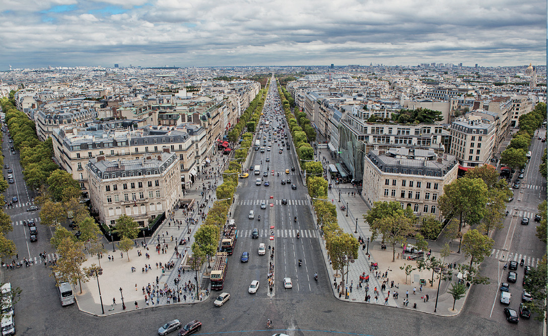 Imagem: Fotografia. Ruas paralelas com vários automóveis. Entre elas há árvores, prédios e casas. Fim da imagem.