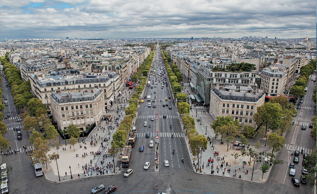 Imagem: Fotografia. Ruas paralelas com vários automóveis. Entre elas há árvores, prédios e casas. Fim da imagem.