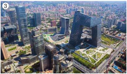 Imagem: Fotografia 3. Vista aérea de vários prédios altos. Em volta há árvores, ruas e casas.   Fim da imagem.