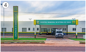 Imagem: Fotografia 4. Uma ambulância parada na frente de uma construção grande. Ao lado, placa com a informação: HOSPITAL MUNICIPAL.  Fim da imagem.