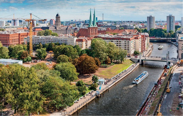 Imagem: Fotografia 4 (ZONA TEMPERADA DO NORTE). À direita, embarcações e pontes em um rio. À esquerda, construções e árvores.  Fim da imagem.