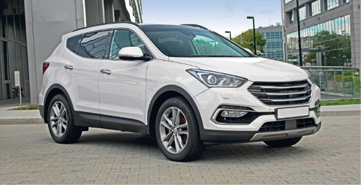 Imagem: Fotografia. Um carro branco com detalhes pretos. Ao fundo, prédios e árvores.  Fim da imagem.