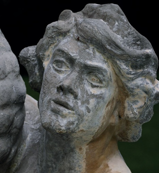 Imagem: Fotografia. Escultura de uma pessoa com cabelo encaracolado e curto. Na lateral do rosto há manchas marrons. Fim da imagem.