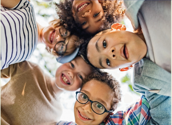 Imagem: Fotografia. Vista de baixo. Destaque para o rosto de cinco crianças sorrindo.  Fim da imagem.