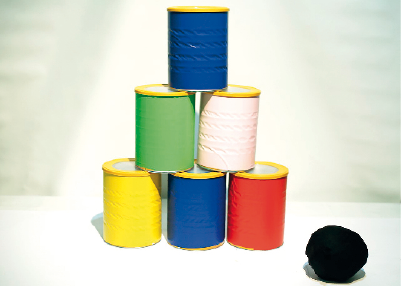 Imagem: Fotografia. Latas coloridas empilhadas. Ao lado há uma bola de tecido preto.  Fim da imagem.