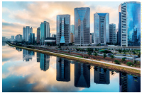 Imagem: Fotografia b). À esquerda, um rio. À direita, diversos prédios espelhados.  Fim da imagem.