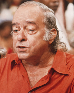 Imagem: Fotografia. Vinícius, homem calvo com cabelo grisalho, olhos pequenos, nariz arredondado e lábios finos. Fim da imagem.