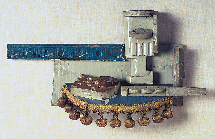 Imagem: Escultura. Na parte superior, um retângulo de madeira cinza e ao lado há uma faixa de madeira azul. Na parte inferior há um semicírculo com estofamento azul e franjas douradas. Fim da imagem.