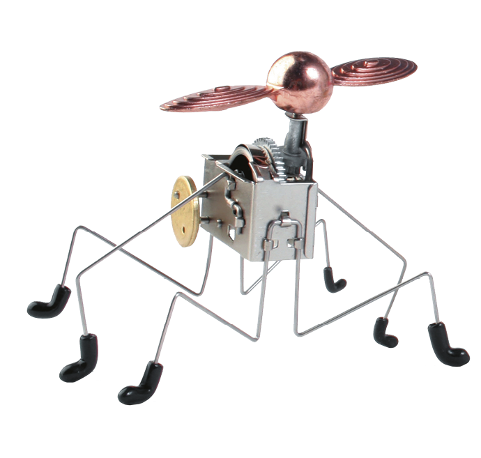 Imagem: Fotografia. Brinquedo com formato de inseto. No centro há uma estrutura comprida de metal prateado e acima há uma esfera rosa com dois aros rosa nas laterais. Abaixo há patas compridas e pretas. Fim da imagem.