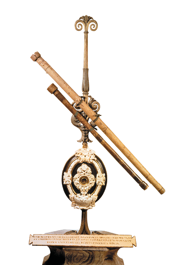 Imagem: Fotografia. Luneta antiga com dois canos finos ligados a base. Fim da imagem.