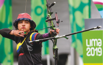 Imagem: Fotografia. Uma mulher usando chapéu e roupas pretas segurando um arco e flecha. Fim da imagem.