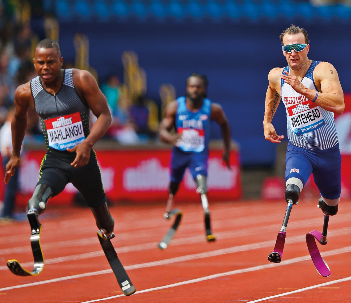 Imagem: Fotografia. Homens com uniformes e próteses nas pernas em uma pista de corrida. Fim da imagem.