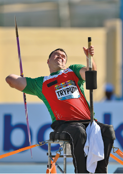 Imagem: Fotografia. Um homem com uniforme, sentado sobre um banco, segurando um dardo com a mão esquerda.  Fim da imagem.