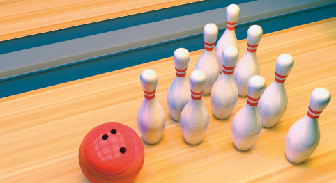 Imagem: Fotografia. Uma bola de boliche com três furos, ao lado pinos brancos enfileirados.  Fim da imagem.