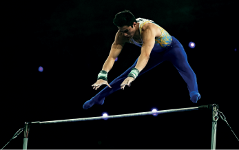 Imagem: Fotografia. Um homem com collant com as mãos próximo a uma barra.  Fim da imagem.