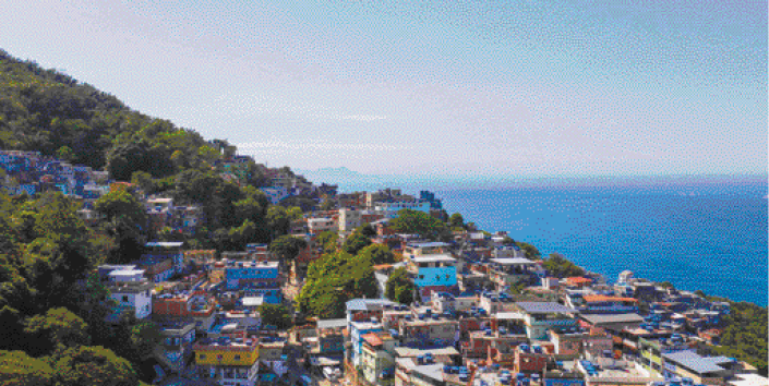 Imagem: Fotografia. Uma cidade em um morro ao lado do mar. O céu está azul e sem nuvens.  Fim da imagem.