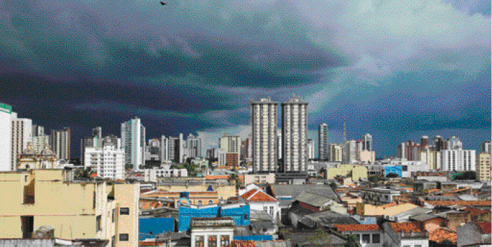 Imagem: Fotografia. Vista aérea de uma cidade com casas e prédios. O céu está nublado.  Fim da imagem.