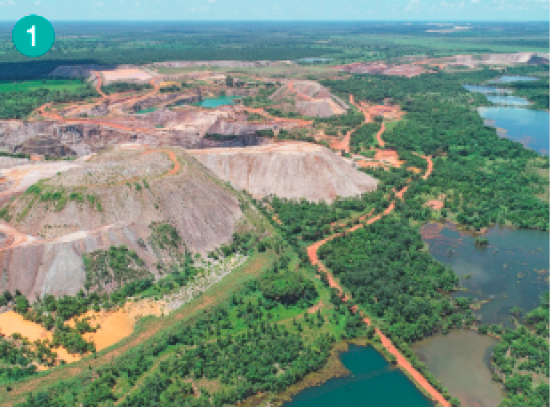 Imagem: Fotografia. Vista aérea de uma área com morros de pedra. Na frente, uma área com árvores ao lado de um rio.  Fim da imagem.