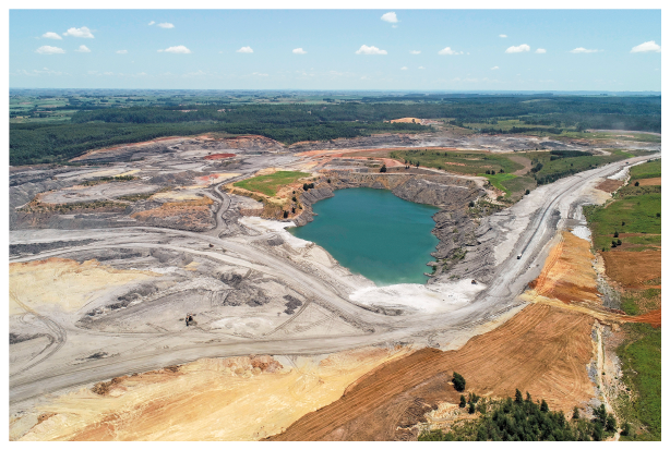 Imagem: Fotografia. Um pequeno lago no meio de uma área desmatada, com partes de terra e partes de pedra.  Fim da imagem.