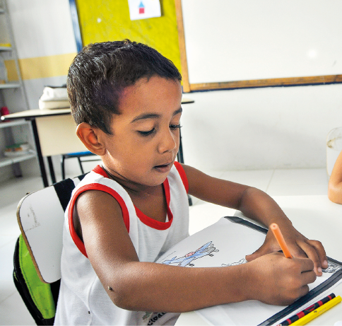 Imagem: Fotografia. Um menino desenha sentado à carteira.  Fim da imagem.