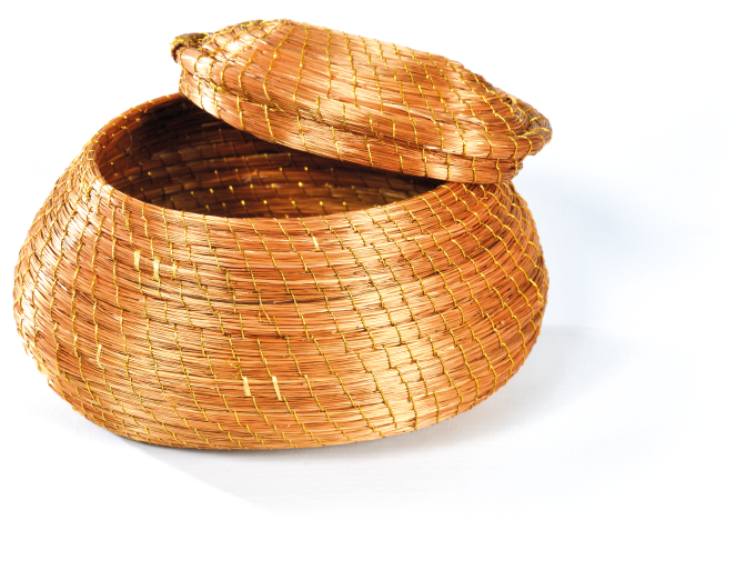 Imagem: Fotografia. Um cesto redondo com tampa feito de fios brilhosos em cor bege e amarrações em dourado.  Fim da imagem.