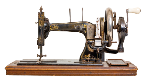 Imagem: Fotografia. Uma máquina de costura que está sobre um suporte de madeira horizontal e apresenta uma parte onde está a agulha e outra extremidade onde fica um círculo ligado a uma manivela.  Fim da imagem.