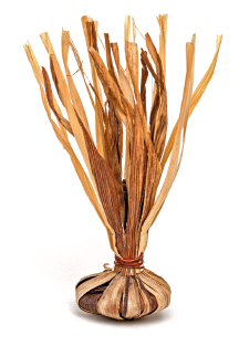 Imagem: Fotografia. Uma peteca que apresenta a parte superior longa com ramificações de palha e a parte inferior redonda, pequena e cheia e também de palha.  Fim da imagem.