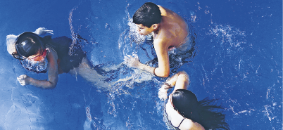 Imagem: Fotografia. Vista aérea de três pessoas dentro de uma piscina. Fim da imagem.