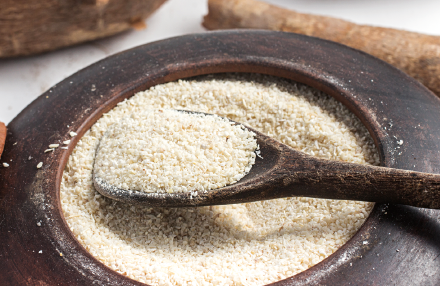 Imagem: Fotografia. Um recipiente cheio de farinha moída de cor clara com um pouco sobre uma colher de madeira.  Fim da imagem.