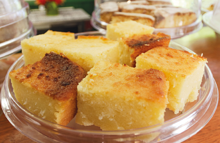 Imagem: Fotografia. Em uma travessa redonda transparente, grandes pedaços de bolo de aspecto amarelo e firme.  Fim da imagem.