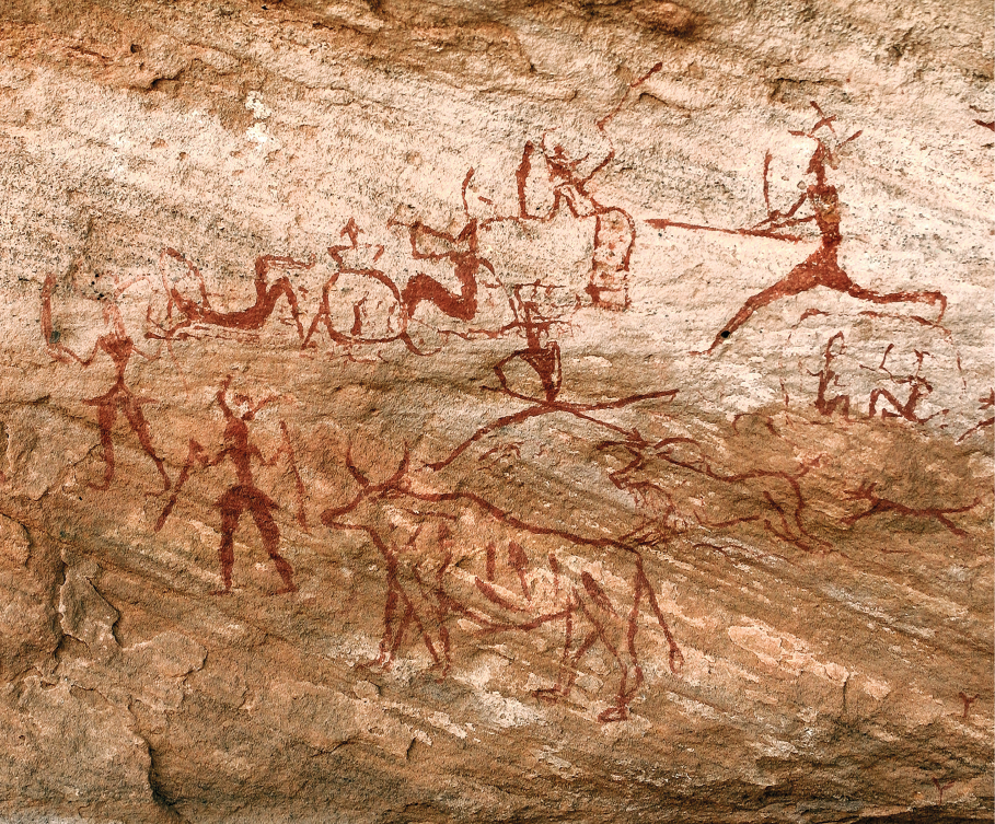 Imagem: Fotografia. Superfície rochosa que apresenta desenhos de animais quadrupedes em movimento e figuras humanas que correm com lanças. Fim da imagem.