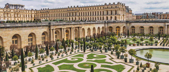Imagem: Fotografia. Destaque do interior de um espaço que apresenta paisagismo no amplo jardim que é contornado por uma construção extensa, com muitos andares, com janelas arqueadas e fachada com tijolos aparentes.   Fim da imagem.