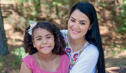 Imagem: Fotografia. Retrato de uma mulher e uma criança que sorriem para foto.  Fim da imagem.