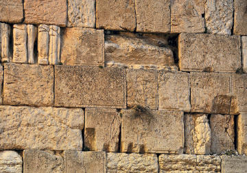 Imagem: Fotografia. Uma parede que apresenta blocos em tons amarelos, alguns estão inteiros e outros lascados. Fim da imagem.