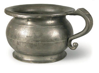 Imagem: Fotografia. Um objeto em formato ovalar, cavidade redonda e interior oco com um pegador lateral e superfície prateada. Fim da imagem.